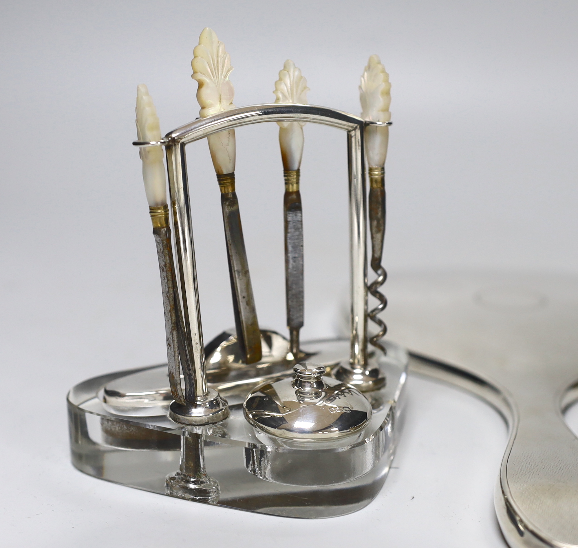 A George V silver mounted glass manicure stand with six accessories, height 12.5cm, a similar silver mounted hand mirror and brush.